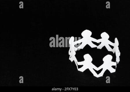Circle of human figures made of white paper over a black surface. Stock Photo