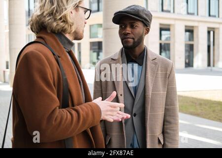 Young man in coat talking to his colleague while they standing in the city Stock Photo
