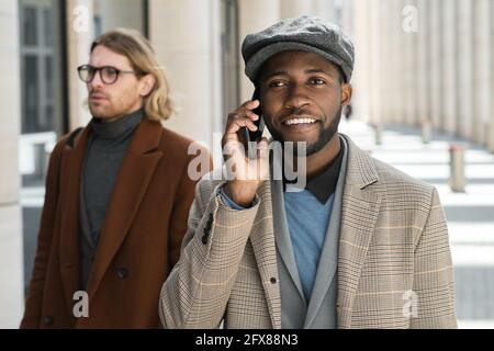 African smiling businessman talking on mobile phone while walking along the street Stock Photo