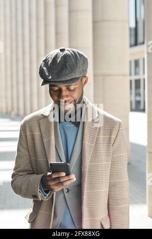African young man looking at mobile phone in his hand and smiling standing outdoors Stock Photo
