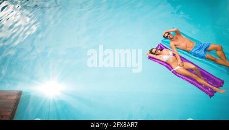 Composition of couple lying on inflatables in swimming pool with glowing light and copy space Stock Photo