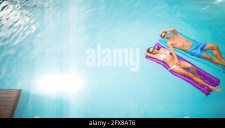 Composition of couple lying on inflatables in swimming pool with glowing light and copy space Stock Photo