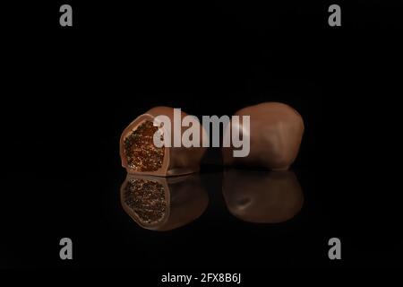 Chocolate candies on a dark background with reflection. Piece by piece and as a whole. Filling of nuts and fruits. Copy space. Stock Photo