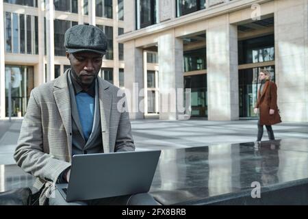African businessman typing on laptop and working online while sitting in the city Stock Photo