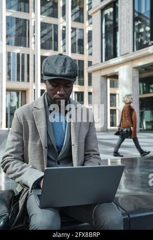 African man sitting outdoors and typing on laptop he working online Stock Photo
