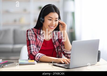 Distance Learning. Cheerful Asian Woman In Headset Studying With Laptop At Home Stock Photo