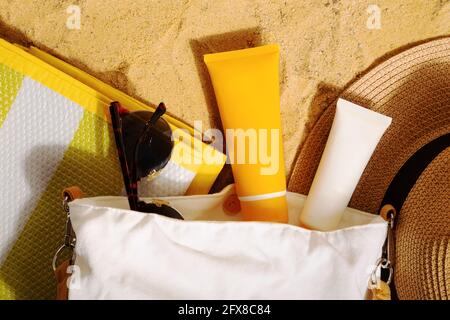 Orange and white tubes of sunscreen in bag on beach next to straw hat, sunglasses and mat. Sun protection on vacation. Top view Stock Photo
