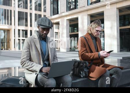 Young businessmen using laptop and mobile phone in the work while sitting in the city Stock Photo