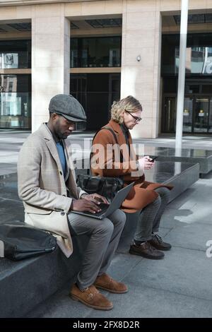 Young people using gadgets and working online while sitting outdoors Stock Photo