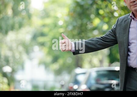 Close-up of businessman in jacket standing at road and catching taxi with thumb-up gesture Stock Photo