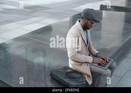 African young businessman working online on laptop computer while he sitting outdoors Stock Photo