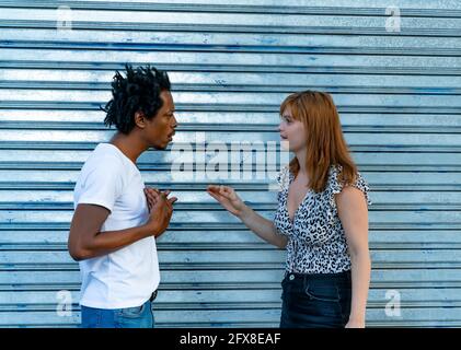Unhappy mixed-race couple arguing on the street front of a metal background. Stock Photo