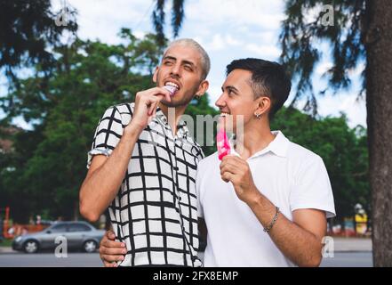 Happy Latin American gay couple having icecream in a city park. Stock Photo