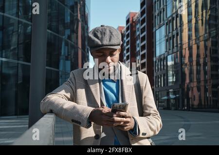 African businessman in stylish clothes communicating online on mobile phone while standing in the city Stock Photo