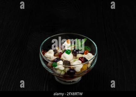 Salad from grapes apples pears kiwi oranges with mascarpone chease and cream. Healthy fresh fruit summer salad in glass bowl on black wooden backgroun Stock Photo