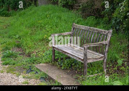 An old distressed wooden park bench set in a church yard in mid Norfolk England Stock Photo