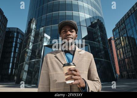 Portrait of African young man drinking coffee from disposable cup and looking at camera in the city Stock Photo