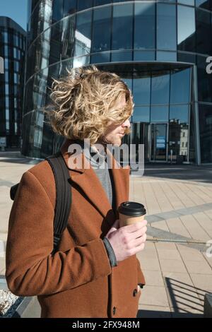 Young man holding disposable cup with coffee while walking outdoors Stock Photo