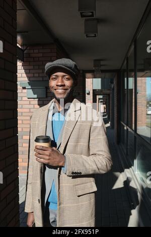 Portrait of happy African man smiling at camera and drinking coffee standing outdoors Stock Photo