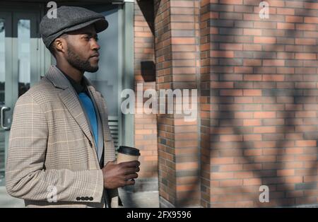 African man holding disposable cup of coffee while walking outdoors Stock Photo