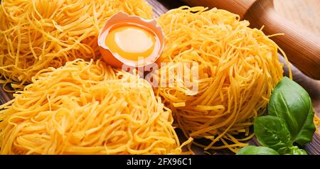 Tagliatelle pasta is thin. Traditional Italian named Angel Hair. Italian egg pasta, homemade and fresh on a wooden table. Rustic cuisine of the north of Italy. Copy space . Banner Stock Photo