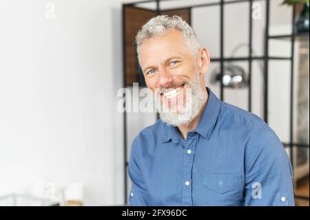 Portrait of charismatic senior middle aged man in smart casual shirt, handsome mature bearded businessman ceo looks at the camera with toothy smile Stock Photo