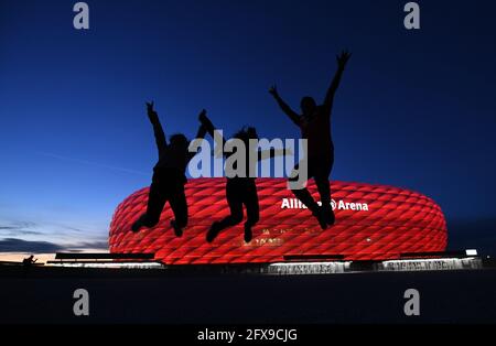 08 May 2021, Bavaria, Munich: Three fans jump up in front of the Allianz Arena after the match in the Bundesliga soccer match FC Bayern Munich - Borussia Mönchengladbach. Some fans have gathered outside the stadium. The new Corona regulations for entries from Great Britain could also bring worries to the European Championship venue Munich. If the stricter measures remain in force until the beginning of July and UEFA, as tournament organiser, does not obtain an exemption, the quarter-finals at the Allianz Arena on 2 July would be in jeopardy. One of the participants in the knockout match would Stock Photo