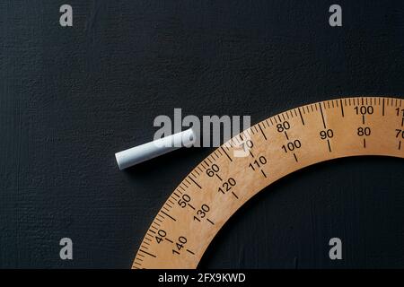 high angle view of a piece of chalk and a wooden protractor on a dark gray chalkboard Stock Photo