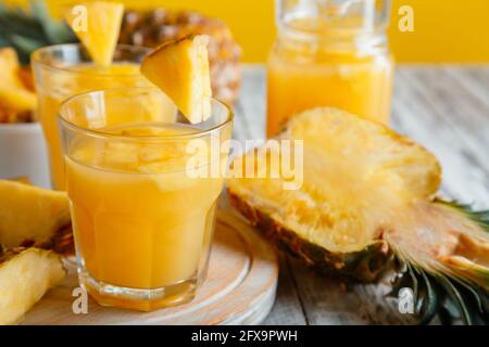 Tasty pineapple juice in glass with pineapple fruit slices. Fresh natural pineapple cocktail and juice in glass on white wooden table. Stock Photo