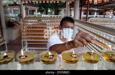 Kuala Lumpur, Malaysia. 26th May, 2021. A devotee wearing a face mask lights an oil lamp in an empty Buddhist temple during the Wesak Day celebration.The Wesak day, commemorates the birth, enlightenment and the passing away of Gautama Buddha, celebrated by Buddhists around the world. Malaysian has adopted a new way of celebrating Wesak Day with the Movement Control Order enforcement, all social and religious gathering are strictly prohibited. (Photo by Wong Fok Loy/SOPA Images/Sipa USA) Credit: Sipa USA/Alamy Live News Stock Photo