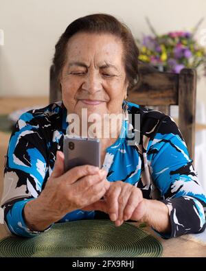 Elderly hispanic woman happily using her smartphone Stock Photo