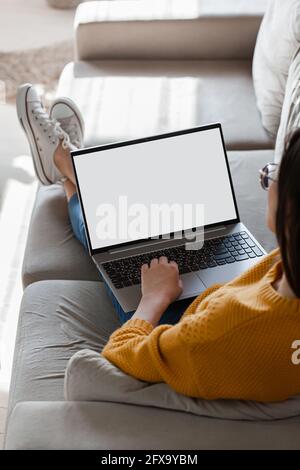 Young woman using laptop screen blank, mockup lying on sofa at home Stock Photo