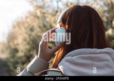 Close up of caucasian young woman listening music with headphones on sunny day while walking in city park Stock Photo