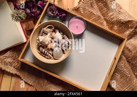 A romantic image of a wooden tray with a bowl filled with seashells, a pink candle, and dried pink roses on a wooden table Stock Photo