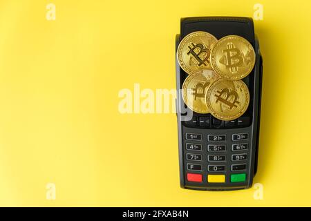 Bitcoin coins on the payment terminal on the yellow background.  Stock Photo
