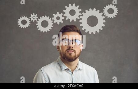 Young businessman thinking about project optimization standing on a gray background. Stock Photo