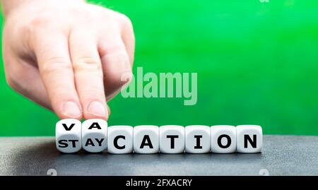 Symbol for normal vacations after the corona pandemic. Hand turns dice and changes the word "staycation" to "vacation". Stock Photo