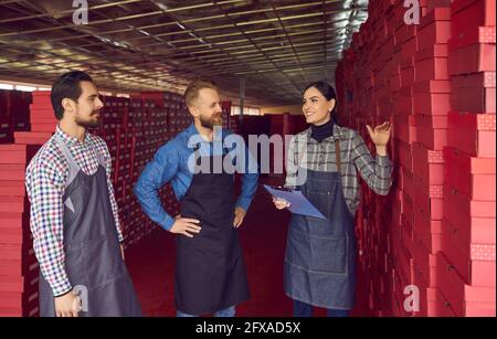 Happy workers talking standing in aisle between stacks of boxes in shoe factory warehouse Stock Photo