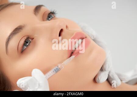 Close up portrait of attractive young woman on procedure injection in lip with special preparation. Concept of process procedure lip augmentation in professional salon. Stock Photo