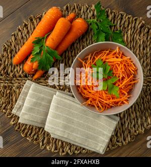Composition of whole and julienned carrots on a straw mat with parsley leaves and beige napkin Stock Photo