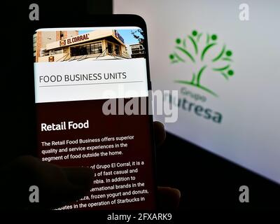Person holding mobile phone with webpage of Colombian food processing company Grupo Nutresa on screen with logo. Focus on center of phone display. Stock Photo