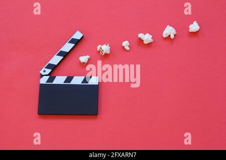 Film clapperboard and popcorn isolated on red background. Entertainment industry. Movie time. Minimalist background. Stock Photo
