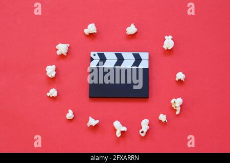 Film clapperboard and popcorn isolated on red background. Entertainment industry. Movie time. Minimalist background. Stock Photo