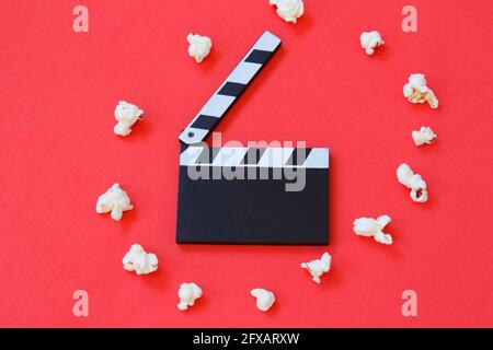 Film clapperboard and popcorn isolated on red background. Entertainment industry. Movie time. Minimalist background. Stock Photo