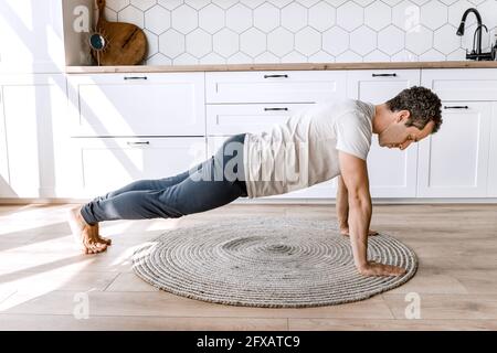 Young athletic attractive man practicing yoga lesson at home on the floor, doing push-ups exercises, standing in plank pose to keep fit Stock Photo