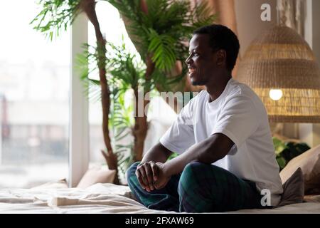 Positive young smiling african man sitting on bed at the morning. Stock Photo