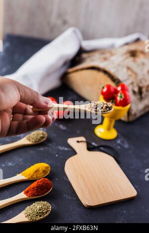 Hand holding a wooden spoon with spices and cherry tomatoes on the table Stock Photo