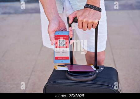Suitcase and smartphone in hand displaying on app mobile expired digital vaccination certificate for Covid-19. Immunity vaccine passport, vaccination Stock Photo