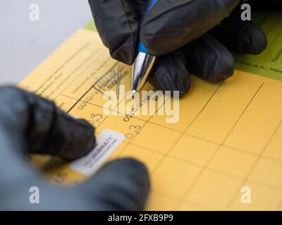 Zurich, Switzerland - 22 May 2021: A medical worker is signing an International Certificate of Vaccination to confirm COVID-19 vaccination (illustration). The International Certificate of Vaccination (here a German version) is also known as Carte Jaune or Yellow Card and is isssued by the World Health Organization (WHO). Stock Photo