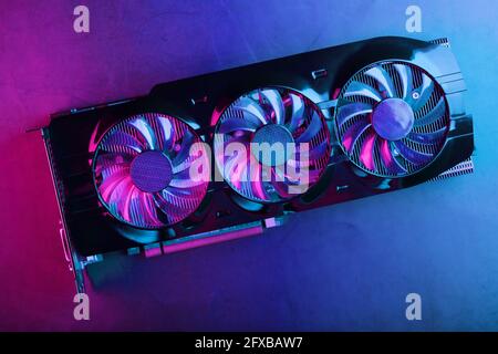 Gaming graphics card with neon magenta-cyan illumination and high-speed fans. Video chip for mining and powerful games in the cyberpunk concept. Stock Photo